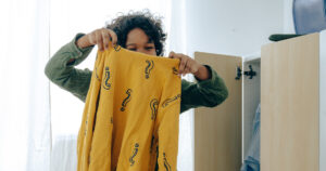 A girl holding up a yellow shirt with question marks on it