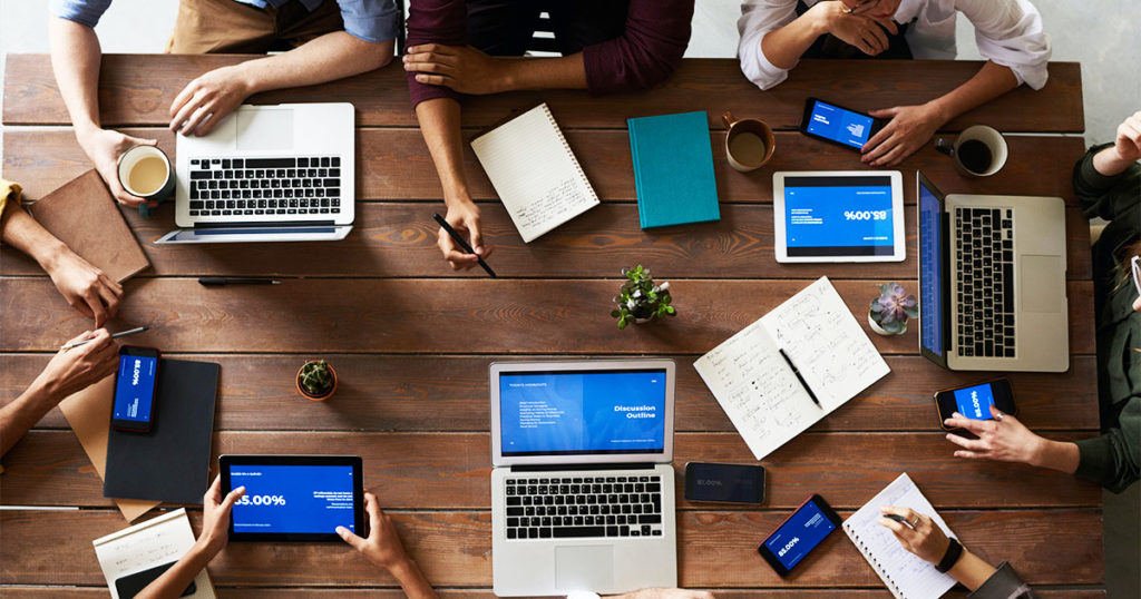 a top down photo of a table with laptops and notebooks with people working around it