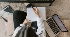 A top down view of someone managing an important virtual agenda with their laptop next to them and notebook