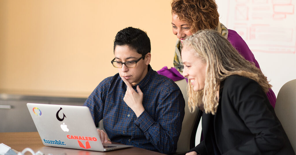 3 people sitting around a laptop engaging and collaborating