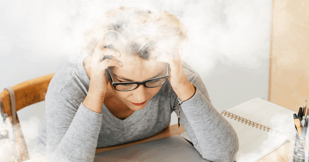 A women with her head in her hands and smoke over her head representing brain fog
