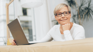 A mature women sitting at a laptop but smiling at the camera.