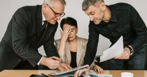 Professional woman experiencing workplace stress while colleagues review documents, illustrating team pressure in the office