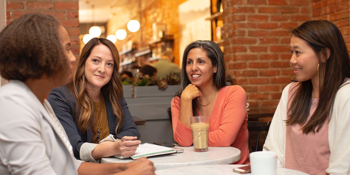 4 mature women sitting at a cafe collaborating, writing down ideas