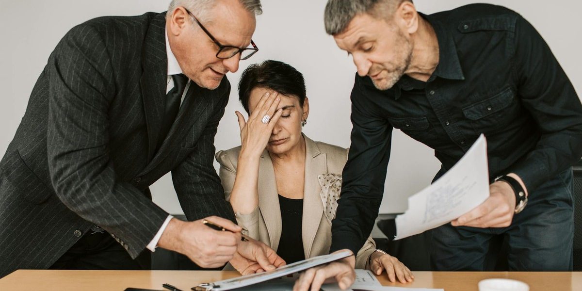 Professional woman experiencing workplace stress while colleagues review documents, illustrating team pressure in the office